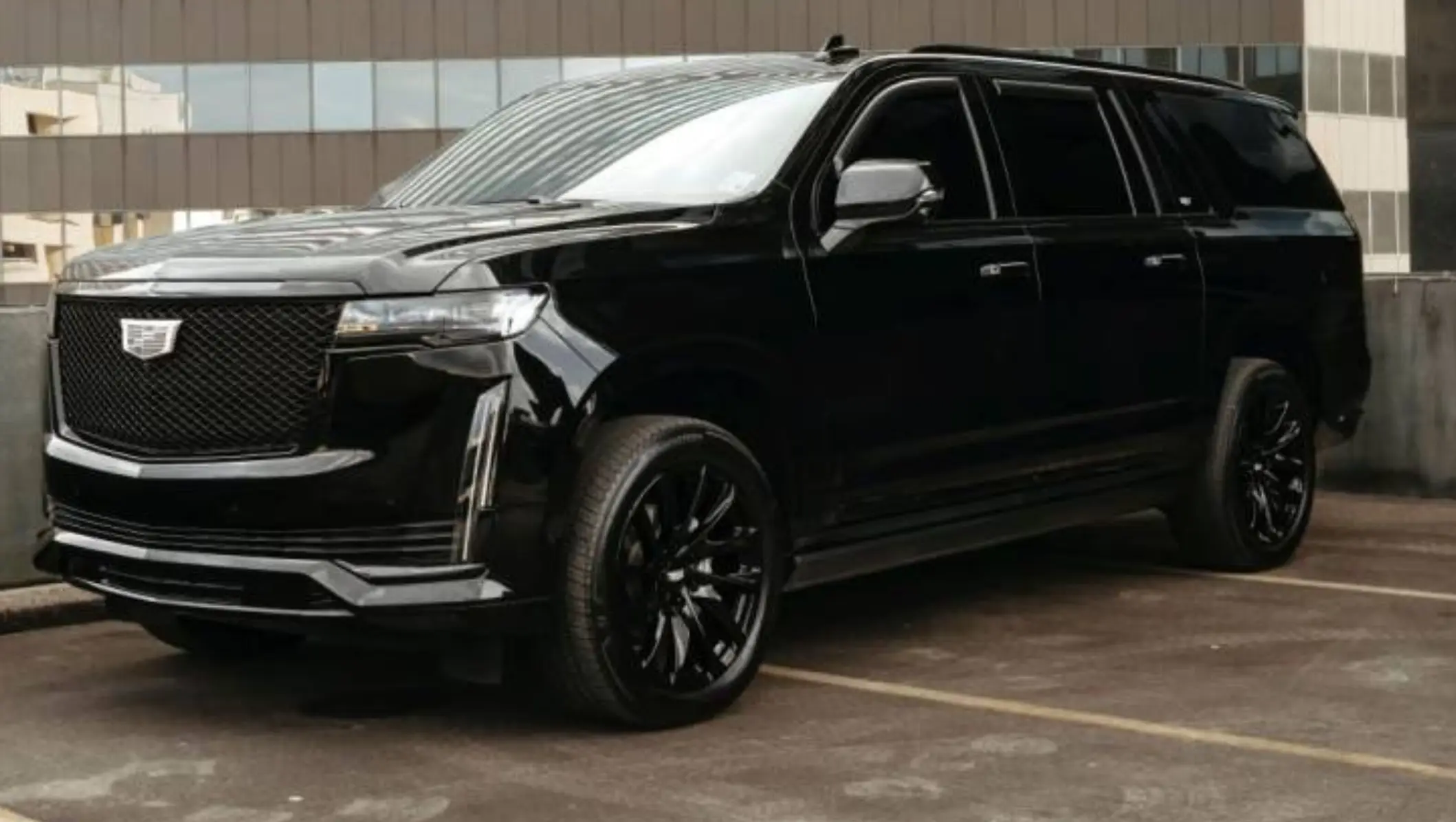 A black suv with its front end in the parking lot.