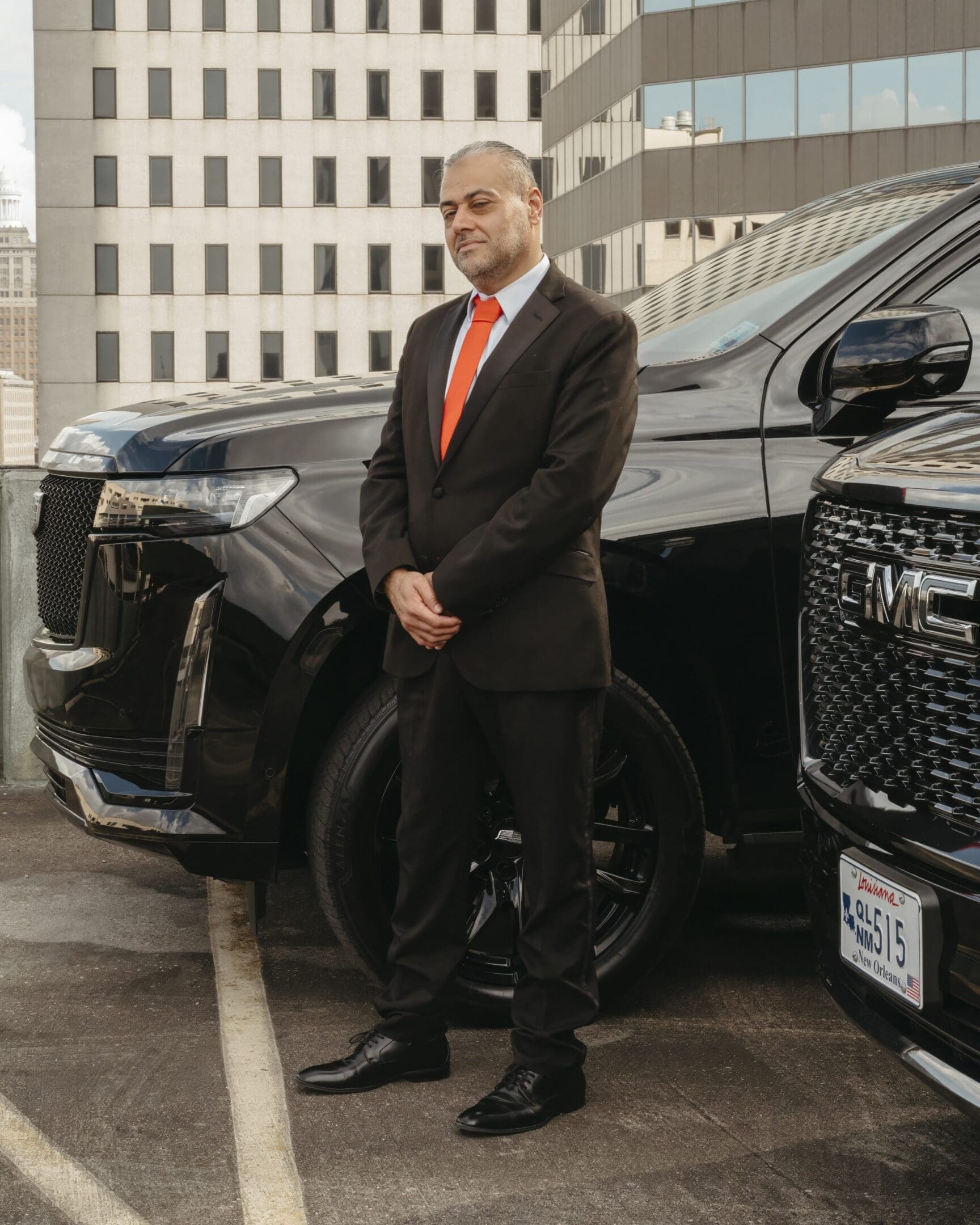 A man in suit standing next to two cars.