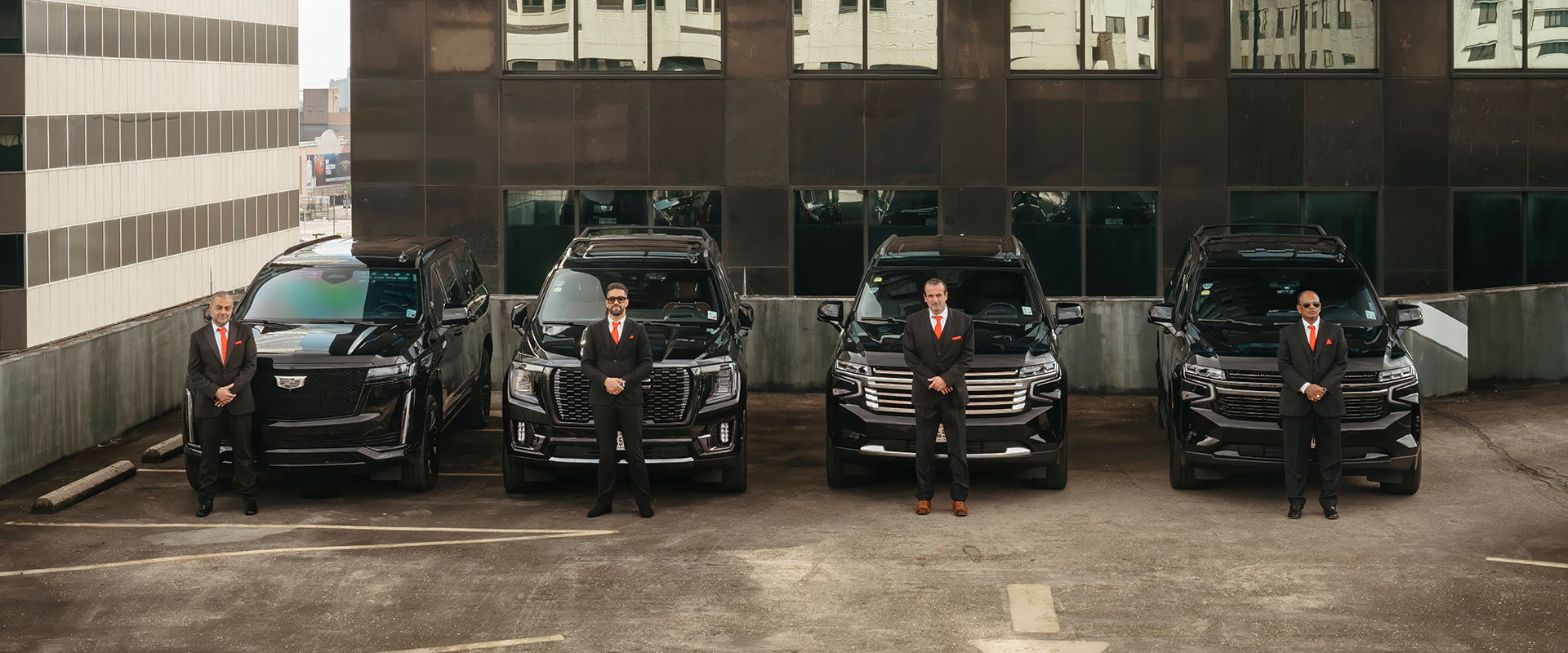 Two men in suits and ties standing next to a line of cars.